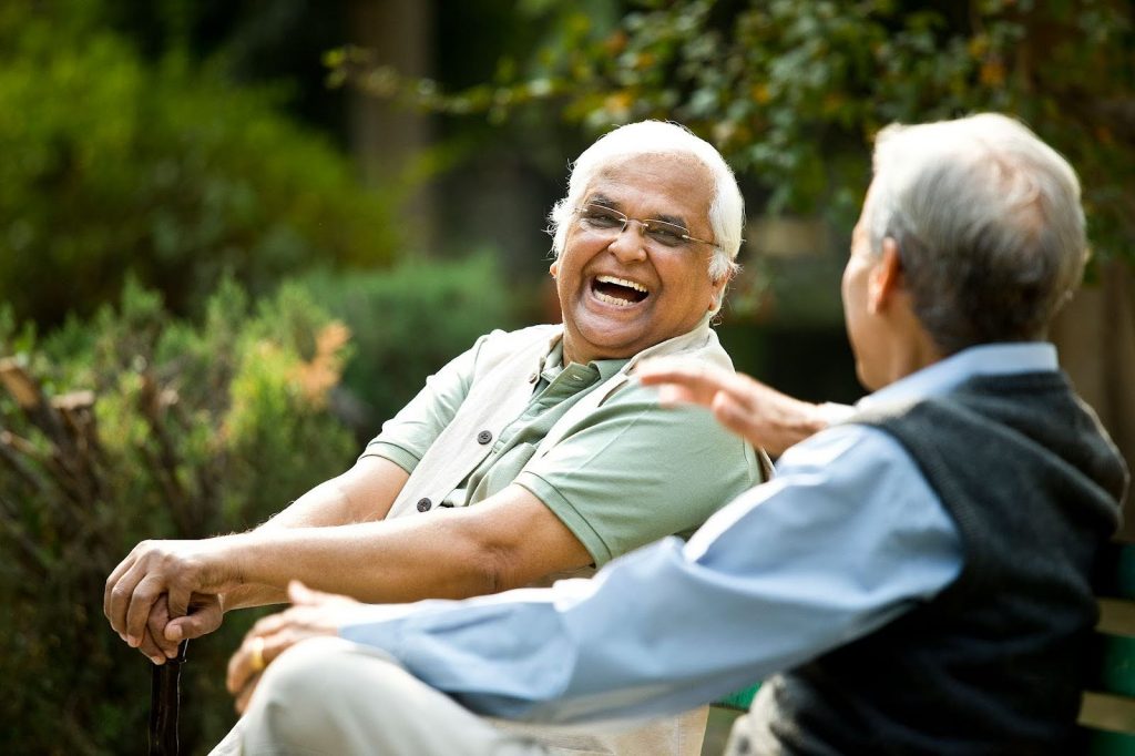 Two senior males laughing on a park bench