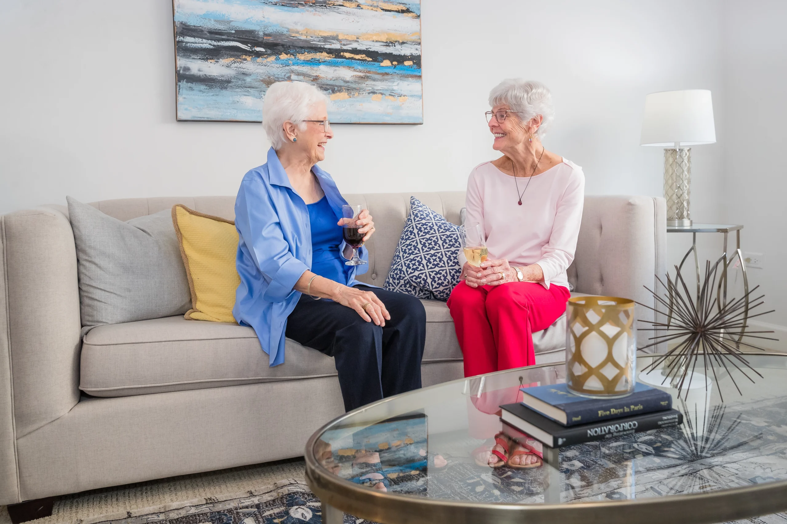 two senior woman talking on a couch while drinking wine and discussing independent living options at Wyndemere in Wheaton, IL.