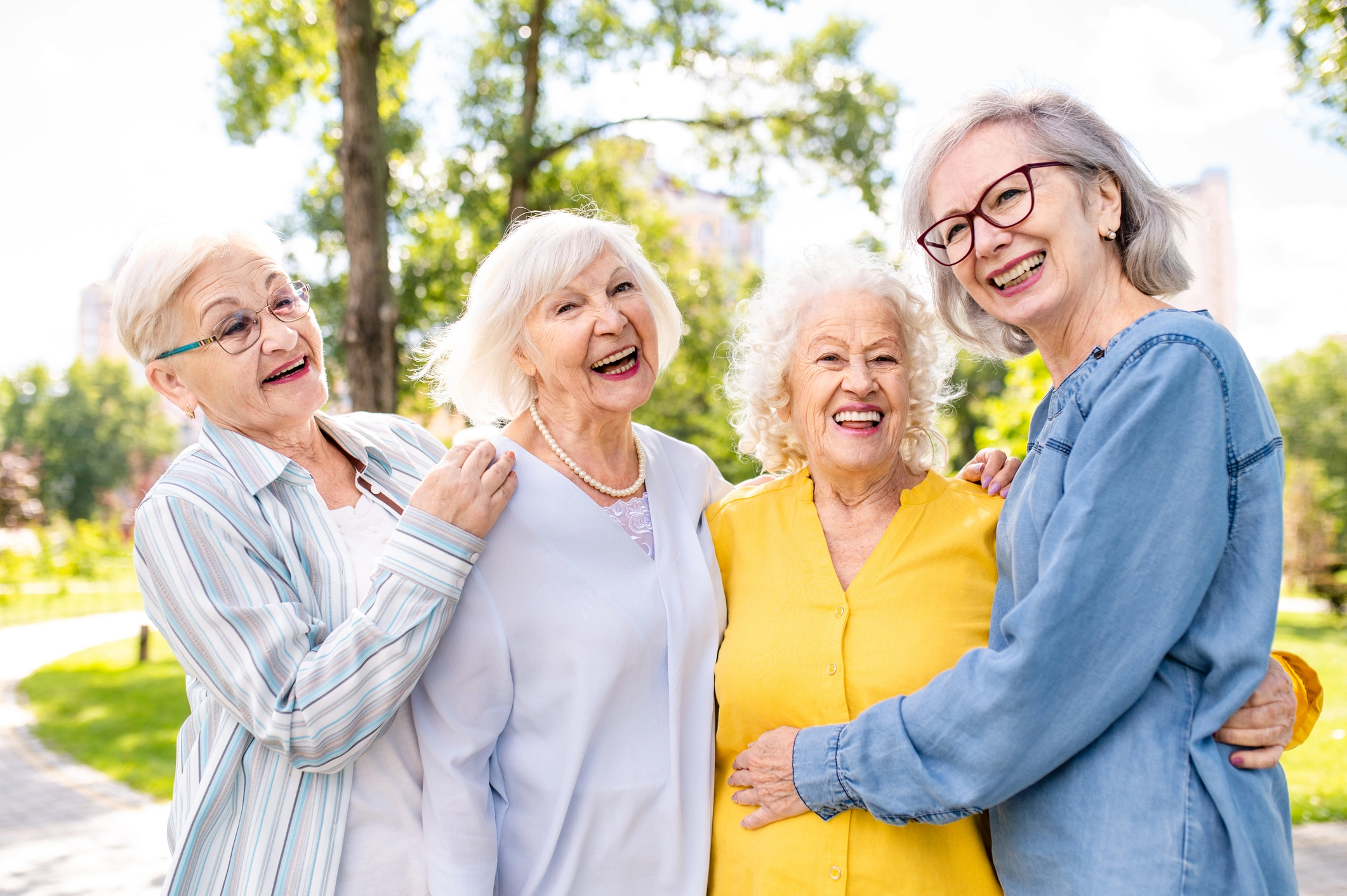 Four women residents of Wyndemere in Illinois hugging and smiling, showing residents always find things to do in Wheaton for seniors.